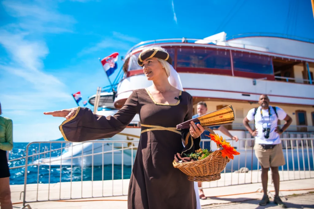 Local host welcoming Zantium Travel cruise guests beside a small ship on the Croatian coast in Korčula
