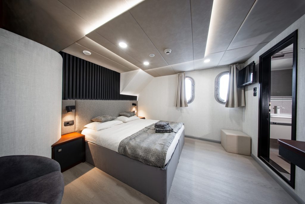 Modern lower deck cabin with a double bed, sea-view portholes and private bathroom aboard a Zantium Travel small-ship cruise in Croatia.