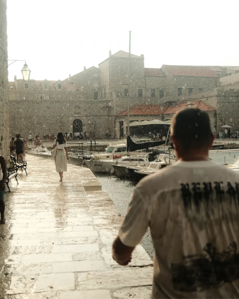 Rain falling over Dubrovnik Old Harbour with small boats and the historic city walls in the background.