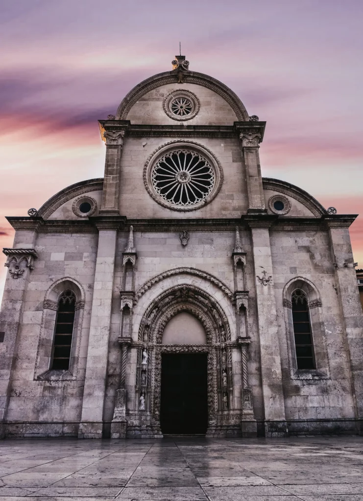 Front façade of St. James Cathedral in Šibenik, Croatia, beneath a pink evening sky.